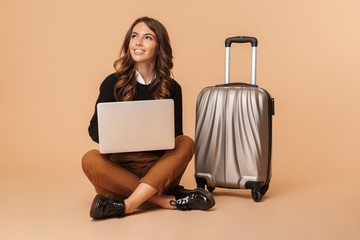 Sticker - European woman with baggage using laptop, while sitting on floor isolated over beige background