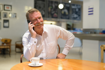 Happy senior businessman sitting while talking on phone at the coffee shop