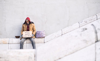 Wall Mural - Homeless beggar man sitting in city holding cardboard sign. Copy space.