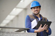 © goodluz - Attractive builder outdoors with tablet and blueprints smiling at camera