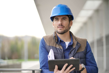 Handsome building expert in hardhat outdoors with tablet and blueprint