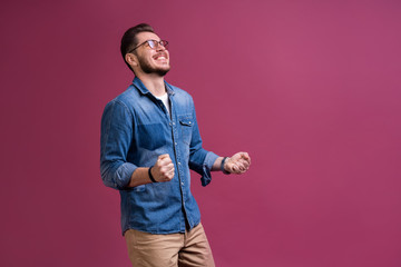 Portrait of a satisfied young man celebrating success isolated over pink background.