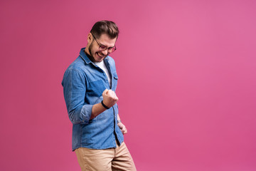 Portrait of a satisfied young man celebrating success isolated over pink background.