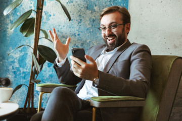 Canvas Print - Smiling businessman wearing suit holding mobile phone