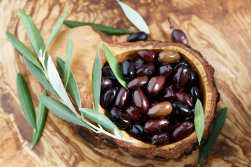 Wall Mural - Fresh brown kalamata olives and olive tree leaves in authentic greek wooden bowl with bark, close up view