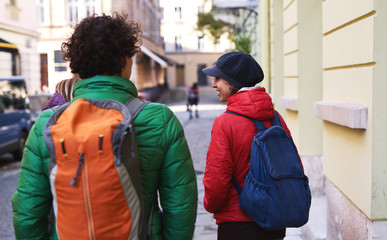 Wall Mural - group of tourists walking on the streets of Lviv. back view of Happy smiling woman with friends tourists in warm outdoor wear walking outdoors at autumn or spring day