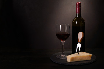 Wine bottle, glass with red wine and cheese on dark wooden background. Celebration concept. Copy space