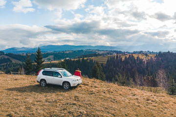 Wall Mural - man in red coat near white suv car at hill with beautiful mountains view