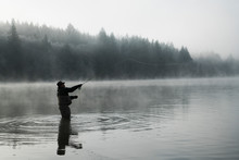 Silhouette Of Fisherman Fly Fishing For Salmon And Sea Run Cutthroat Trout In Puget Sound Near Olympia, Washington USA.