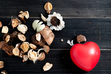 The red heart whit dried leaves and flower is placed on the left side of the black wood table.concept of love and valentine day. Copy space for text and content