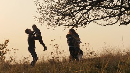 Wall Mural - Happy kids rushes into hands of parents. Parents hugs their kids in the meadow.