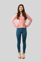 Wall Mural - Full body of Teenager girl with pink shirt posing with arms at hip and laughing looking to the front on isolated grey background