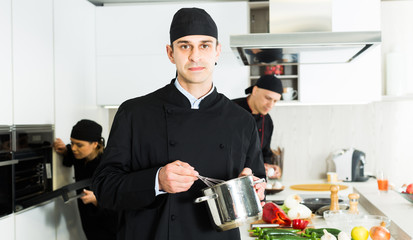 Wall Mural - Portrait of man cook who is standing with pot for soup on his work place in the kitchen