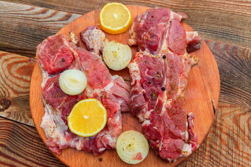 Fresh raw pork meat with spices, lemon and onion on wooden cutting board on rustic table. Top view