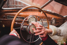 Hands Of The Bride And Groom On The Steering Wheel Of A Retro Car. Vintage Car Inside