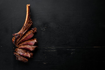 Steak on the bone. tomahawk steak On a black wooden background. Top view. Free copy space.