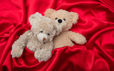 Wall Mural - Love, concept, tight hug. Two teddy bears embracing as a couple in bed, red satin background