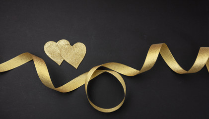 Wall Mural - valentines day. top view of two golden hearts with satin ribbon against black background