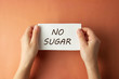 © Inga - No Sugar inscription. Woman holding paper with no sugar lettering in hands isolated brown background. Top view.