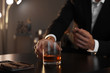 Man with glass of whiskey and cigar sitting at table, closeup. Space for text