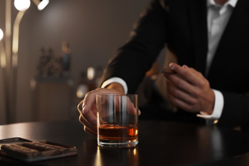 Canvas Print - Man with glass of whiskey and cigar sitting at table, closeup. Space for text