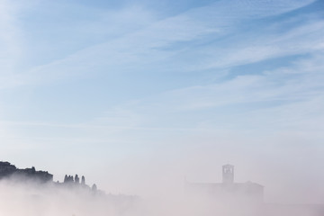 A view of a silhouette of St.Francis church in Assisi in the middle of mist beneath a blue sky with clouds