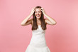 © ViDi Studio - Portrait of joyful laughing bride woman in beautiful white wedding dress standing keeping hands near face isolated on pastel pink background. Wedding celebration concept. Copy space for advertisement.