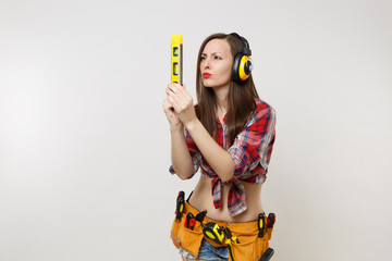 Wall Mural - Pretty handyman woman in plaid shirt, denim shorts, noise insulated headphones, kit tools belt full of instruments hold building bubble spirit level isolated on white background. Female in male work