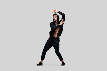 Wall Mural - Young handsome young dancer dressed in black pants, a sweatshirt on a naked torso is dancing street dance. He makes stylized movements with his hands