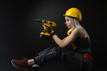 Wall Mural - girl in construction clothes and protective equipment posing with a electric screwdriver