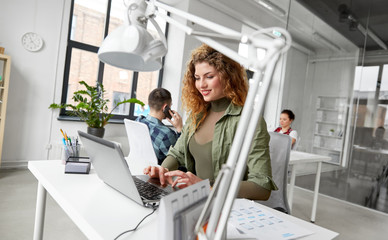 business, technology and people concept - creative woman with laptop computer working on user interface design at office