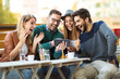 © Mediteraneo - Group of four friends having a coffee together. Two women and two men at cafe talking laughing and enjoying their time using digital tablet.