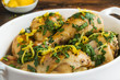 Baked chicken legs with fresh parsley and lemon juice and zest in white casserole on wooden rustic table, close-up