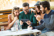 © Mediteraneo - Group of four friends having a coffee together. Two women and two men at cafe talking laughing and enjoying their time using digital tablet.