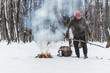 © Sergey - Traveling man makes a fire. Winter time. Concept adventure active vacations outdoor. Extreme camping. vintage backpack and thermos with tea, snowy forest