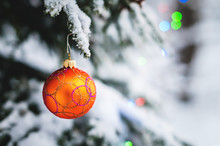 Close-up Of A Christmas Toy On A Snow-covered Lively Tree In The Winter Forest On The Background Of Lights
