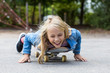 © Westend61 - Smiling girl with blond hair lying on skateboard in playground