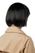 A close up back view side shot of a lady with black blunt bob hairstyle, wearing a beige coat with a collar and epaulettes. The woman is posing against the white background. New-fashioned hairstyle. 