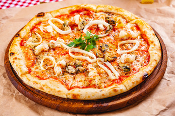 Italian Pizza with seafood and mozzarella cheese on wooden cutting board. Close up