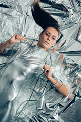 Wall Mural - top view of brunette fashionable girl posing in silver bodysuit and raincoat on metallic background