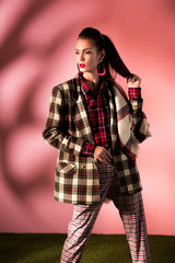 Wall Mural - fashionable girl posing in cozy checkered suit on pink background