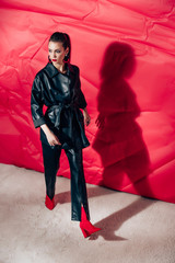 Wall Mural - attractive model posing in black leather suit on red background