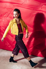 Wall Mural - fashionable girl posing in yellow leather jacket on red background for fashion shoot