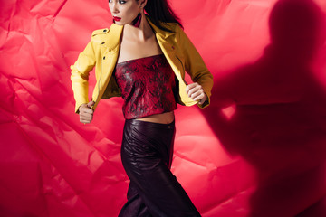 Wall Mural - attractive elegant woman posing in yellow leather jacket on red background