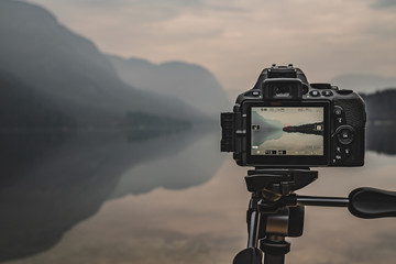 Camera on tripod at work on a misty lakeshore. Camera display. Taking pictures using the display.