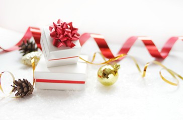 Christmas gift boxes with a red bow, next to the Christmas ball, red ribbon, cones on a white background with snow