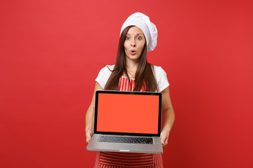 Wall Mural - Housewife female chef cook or baker in striped apron white t-shirt toque chefs hat isolated on red wall background. Woman hold laptop pc blank screen for promotional content Mock up copy space concept