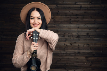 Portrait of a smiling casual woman posing with guitar against wooden plank