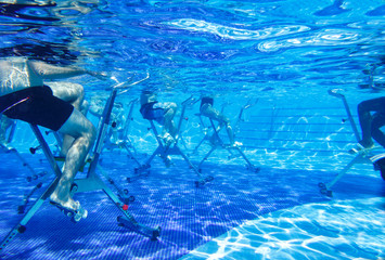 Touristen doing aqua aerobics on exercise bikes in swimming pool tropical hotel