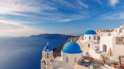 Fototapete - Churches in Oia, Santorini island in Greece, on a sunny day with dramatic sky. Scenic travel background. 4K timelapse.